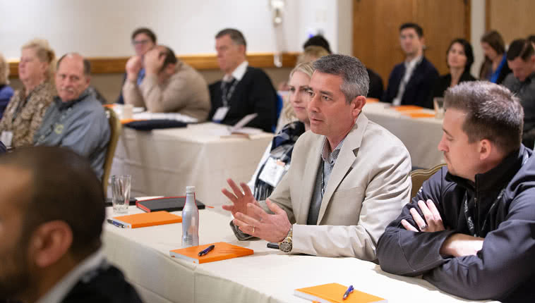 man speaking in a group of people sitting at tables