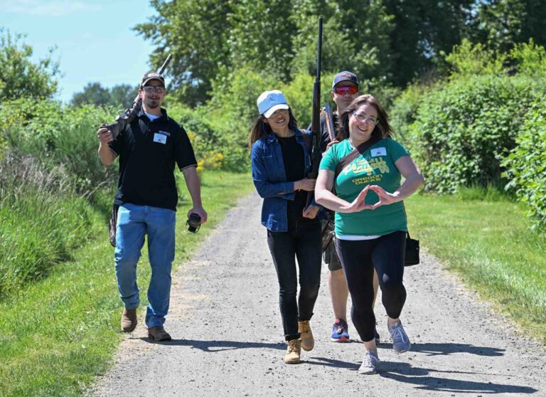 four people walking with shooting equipment, woman making an O with her hands