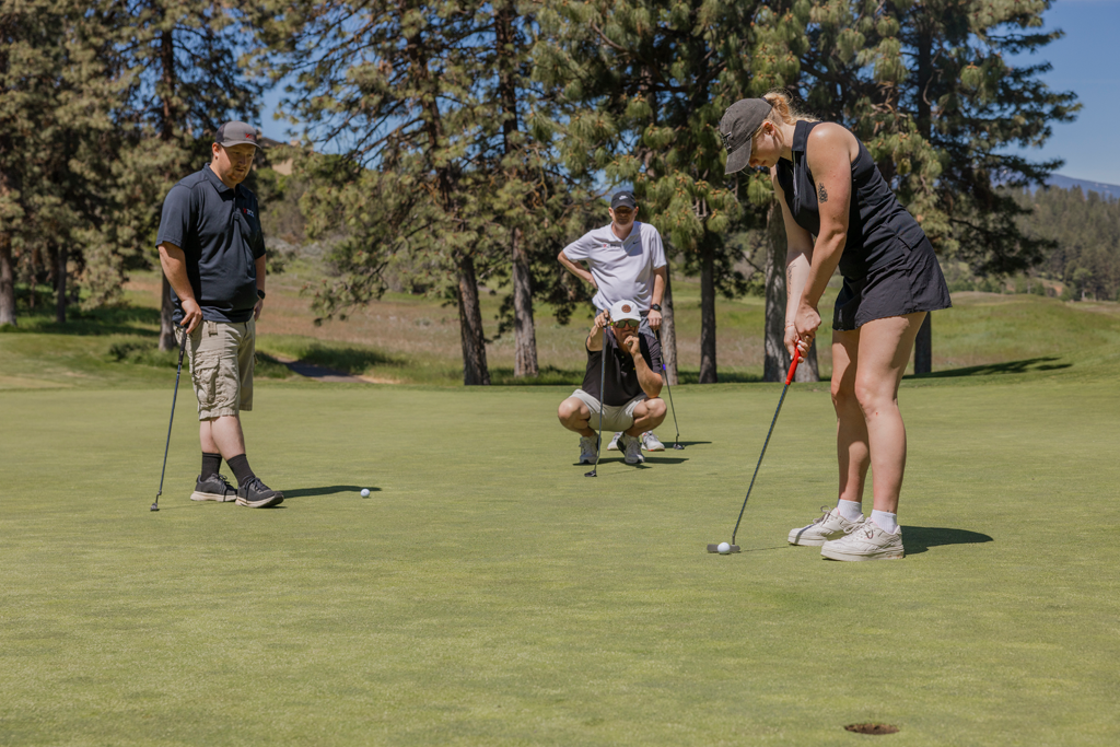 four golfers, one putting, one squatting, and two watching