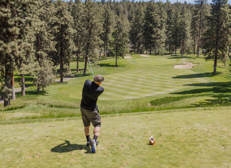 man surrounded by trees hitting golf ball