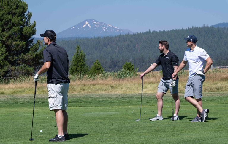 three men with golf clubs and Mt Bachelor in the background