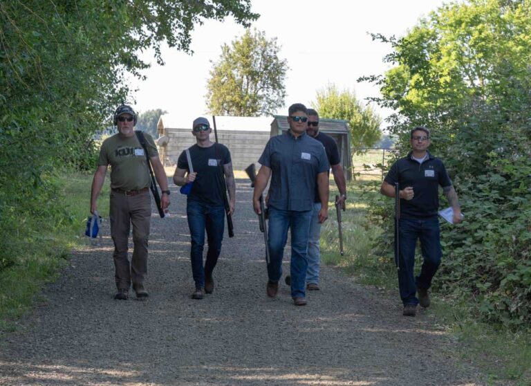 four men walking on a skeet range holding rifles
