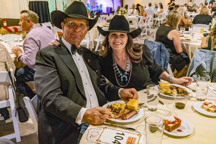 smiling man and woman wearing cowboy hats eating dinner