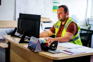 construction worker sitting at a computer in a messy office