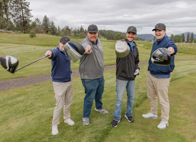 Four men holding golf clubs up to the camera