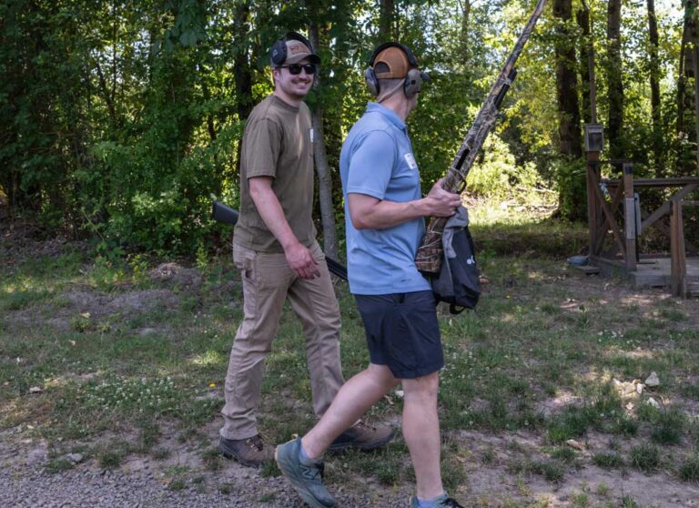 two men walking, one carrying a rifle