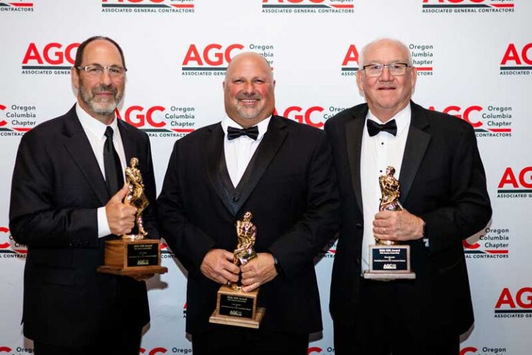 three smiling men holding award statues